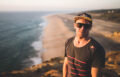 Portrait von Andrew Cotton mit Sonnenbrille und Red Bull Cap mit Strand hinter ihm